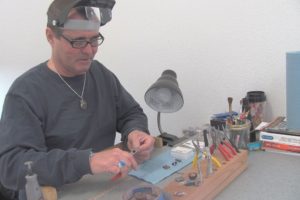 Mark Lewis uses round nose pliers to shape sterling silver wire for a sculptured pendant. He also makes earrings and bracelets, while working with semi-precious stones, Dichoric glass, fossils and cabochons. Lewis recently opened his jewelry store in downtown Washougal.