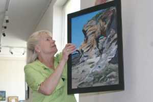 Tulla Burke, historian with the Second Story Gallery Society, hangs "Keyhole Rock II," by Judith Sanders-Wood. The showing of the Ridgefield resident's work opened Friday with a reception at the Second Story Gallery inside the Camas Public Library.