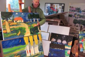 Mike Smith is represented by several galleries, including one in Hilton Head, S.C. Here, he poses with two pastels he is sending to the gallery. In the background are works in progress and a guitar from his Army days.   Horses feature prominently in his work. "Horses embody everything that is cool about the earth," Smith said.