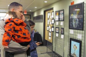 Jeff Snell, Camas School District assistant superintendent, listens to students describe their work at the CHS art show via a recording by dialing a specific number associated with each piece. His daughter, Mackenzie, does the same while son Micah takes a nap.