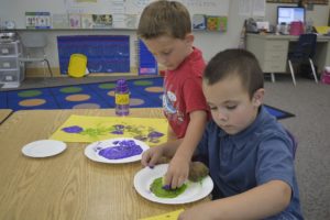 Caleb Plamondon and Joshua Homuth participate in the "Ready, Set, Kindergarten" summer program at Hathaway Elementary School. Here, they paint with vegetable and fruit stamps.  The assignment took several steps to explain and hinged on the students sharing stamps and paint colors.