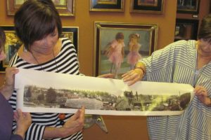 Artist Maria Repetto and downtown Camas art gallery owners Sharon Ballard and Marquita Call (left to right) hold the photograph that is the inspiration for the first mural that will be part of the Camas-Washougal Mural Project. The image of downtown Camas was taken in 1911 or 1912 from Northwest Sixth Avenue and Division Street, according to the picture's owner Brent Erickson. The mural will be painted by Repetto and mounted on a 3 foot by 30 foot space above the entry to the Ballard & Call Fine Art Gallery. The unveiling is expected to occur this fall.