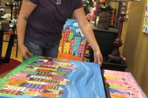 Leah Baker, owner of Anything But Ordinary, looks over acrylic paintings by Janet Bentley-Jones, of Ridgefield. Bentley-Jones is the featured artist this month at the new business in downtown Camas. In addition to art, Baker sells purses, scarves, candles, cards and jewelry.