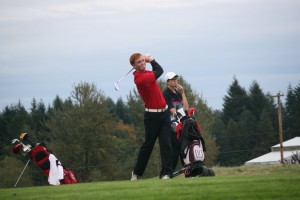 Brian Humphreys tees off on the 14th hole, while Ben Gruher watches in the background, during the 4A district tournament Tuesday, on the Tri-Mountain Golf Course, in Ridgefield.