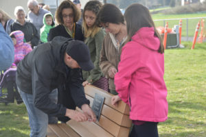 Gause Elementary dedicated its new "Buddy Bench" in honor of teacher Alisa Vail, who passed away in June of 2016, at a ceremony held March 29. Here, Vail's husband, Andy Vail, installs the plaque as Vail's mother, Lori Rasmussen, daughter Annabelle, sister Amee Rasmussen and daughter Abbie look on. (Contributed photo)