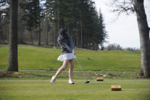 Camas senior Emma Cox powers through the ball and keeps her drive low in the wind in the Papermakers' first league match against Heritage on March 19.  Cox fired a 38 in difficult, windy conditions. 