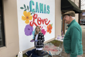 Hailee Parman (left) works on her 'Camas Love' mural in downtown Camas as a passerby comments on the artwork. Parman, a Camas High Senior, has collaborated with Papermaker Pride to have her design featured on a line of clothing being debuted Friday, March 6. (Contributed photo courtesy of Hailee Parman)