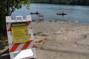 A sign warns toxic algae, which is harmful to humans and pets, is present in Lacamas Lake, as kayakers paddle by, in July 2020. (Kelly Moyer/Post-Record)