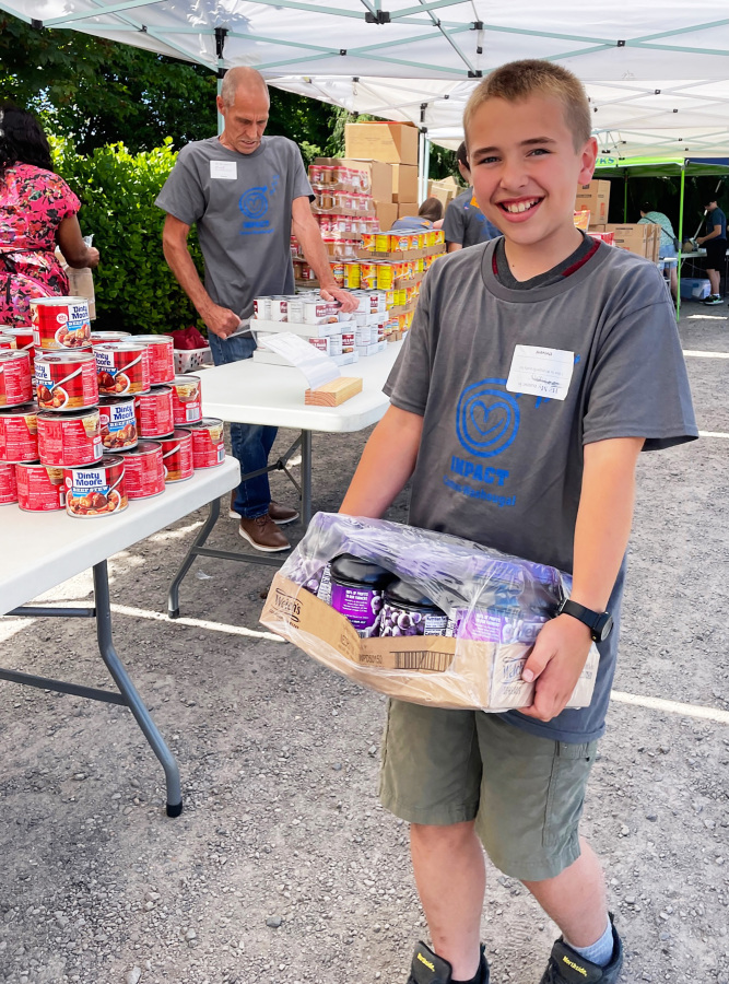 An IMPACT Camas-Washougal volunteer carries a box of canned food at a food box assembly event in 2023.