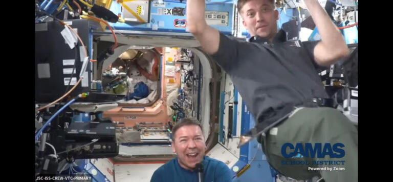 A member of the crew living on the International Space Station (right) floats past NASA astronaut Dr. Michael Barratt (left), a 1977 Camas High School graduate, as Barratt speaks to Camas students via a remote video feed, Thursday, May 23, 2024.