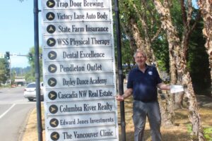 Washougal Business Association President Paul Greenlee extends his arms in disbelief next to the city of Washougal’s wayfinding sign on Main Street, Aug. 1, 2024. (Photos by Doug Flanagan/Post-Record)