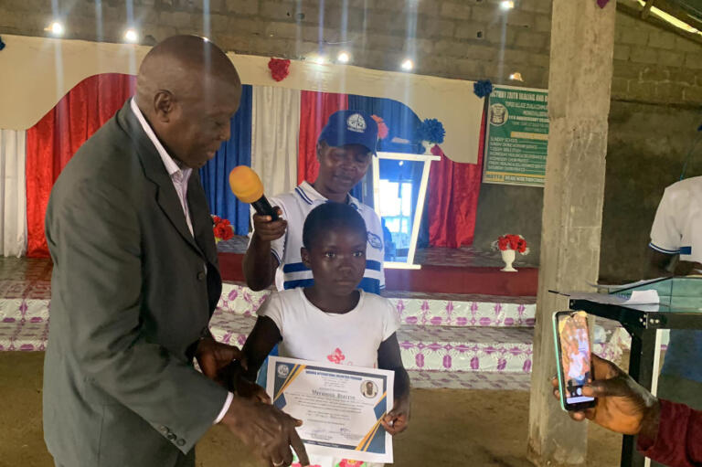 Gabanja International Volunteer Program  board chairman Felix Dordor (left) presents a certificate of completion to a student on July 12, 2024.